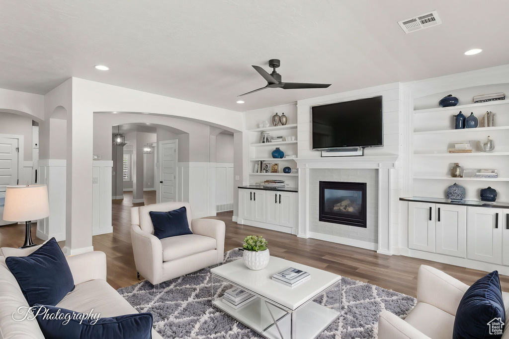 Living room featuring ceiling fan, arched walkways, wood finished floors, built in features, and recessed lighting