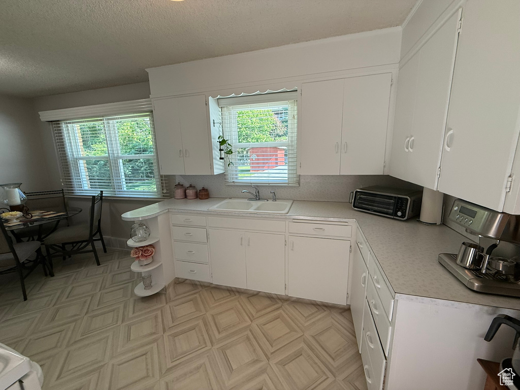 Kitchen with a sink, light countertops, white cabinetry, light flooring, and a textured ceiling