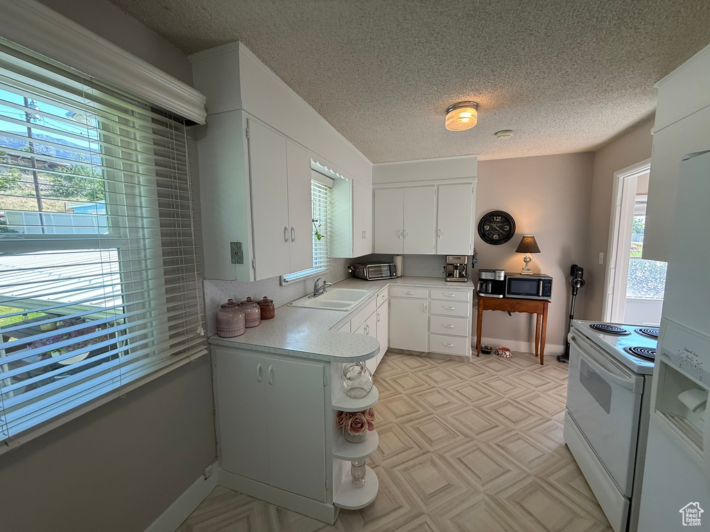 Kitchen with white appliances, a sink, light countertops, white cabinets, and a textured ceiling