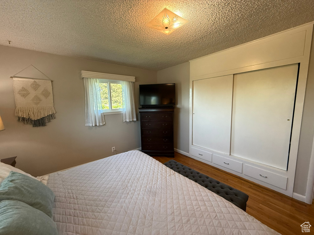 Bedroom featuring wood finished floors, a textured ceiling, a closet, and baseboards
