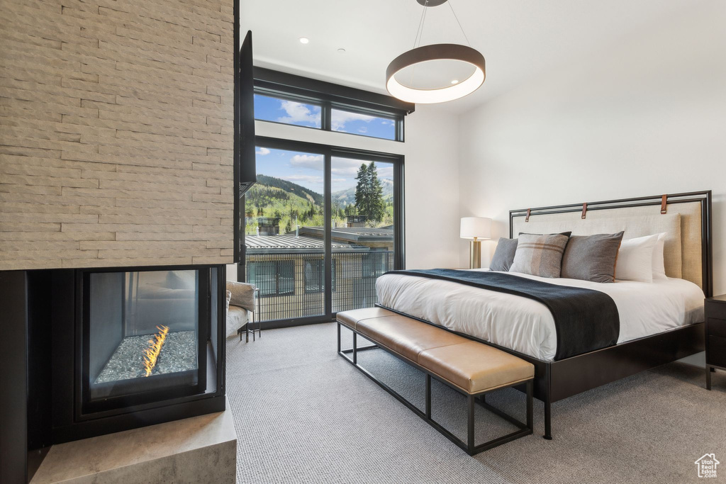 Carpeted bedroom with access to exterior, a high ceiling, a multi sided fireplace, and a mountain view