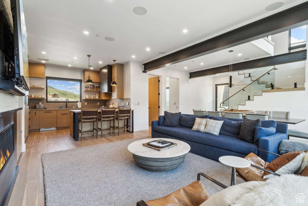 Living room with stairway, light wood-type flooring, a glass covered fireplace, wet bar, and recessed lighting