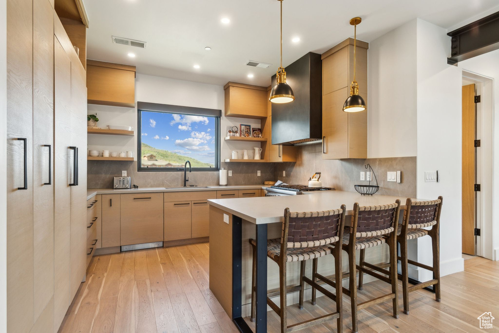 Kitchen featuring wall chimney exhaust hood, open shelves, light wood finished floors, a sink, and light countertops