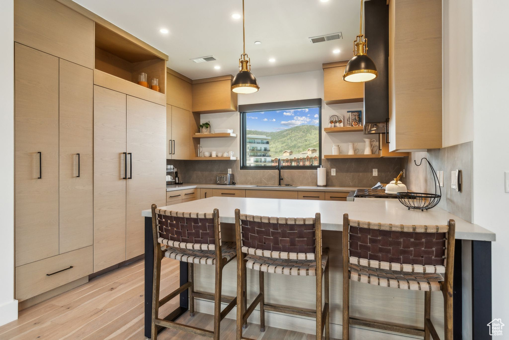 Kitchen with open shelves, a sink, a peninsula, light countertops, and a breakfast bar area