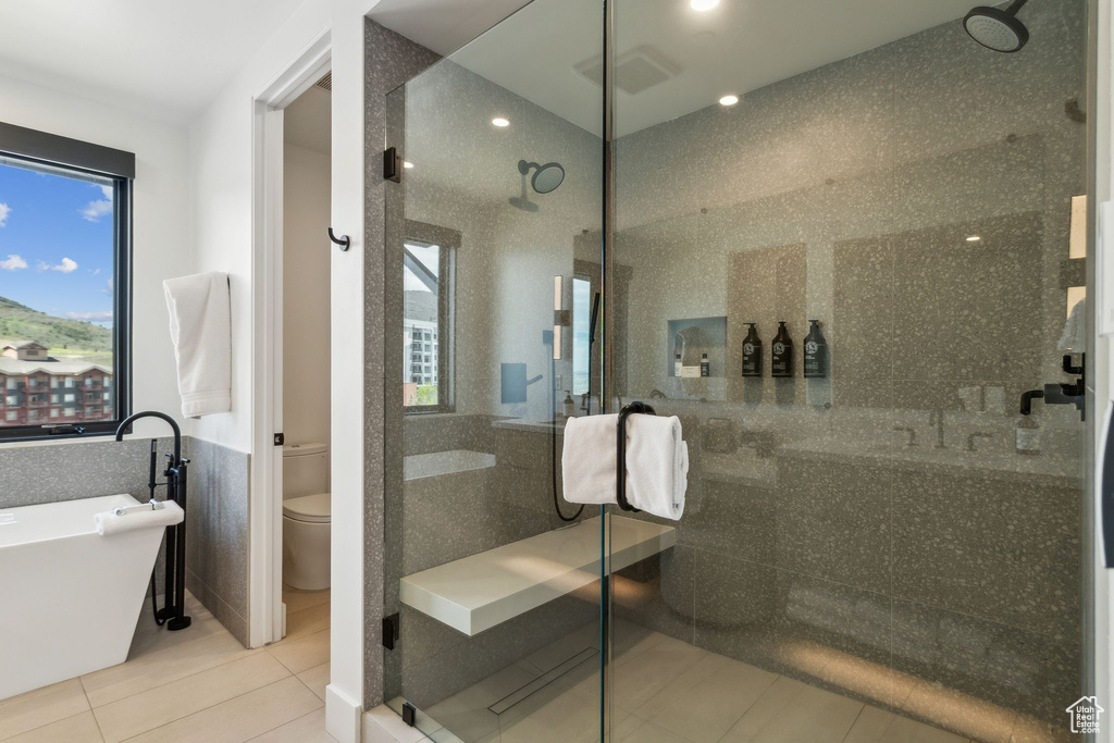 Full bathroom featuring tile walls, toilet, a freestanding tub, a shower stall, and tile patterned floors
