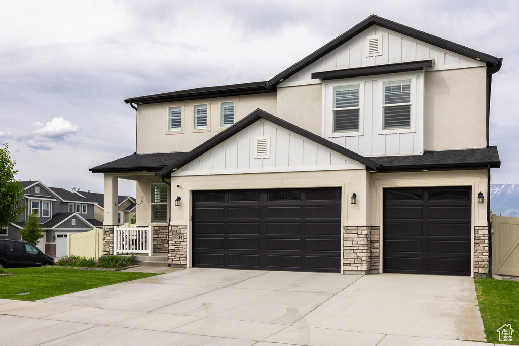 View of front facade featuring stone siding, concrete driveway, board and batten siding, a garage, and a shingled roof