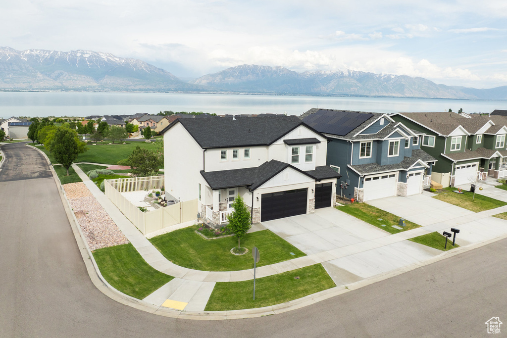 View of front of home with concrete driveway, an attached garage, a residential view, stone siding, and a water and mountain view