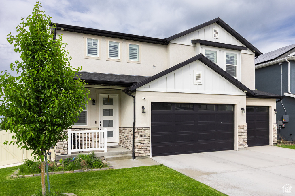Modern inspired farmhouse featuring stone siding, driveway, board and batten siding, and a garage
