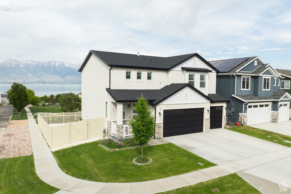 View of front of property with concrete driveway, a water view, stone siding, a garage, and a porch