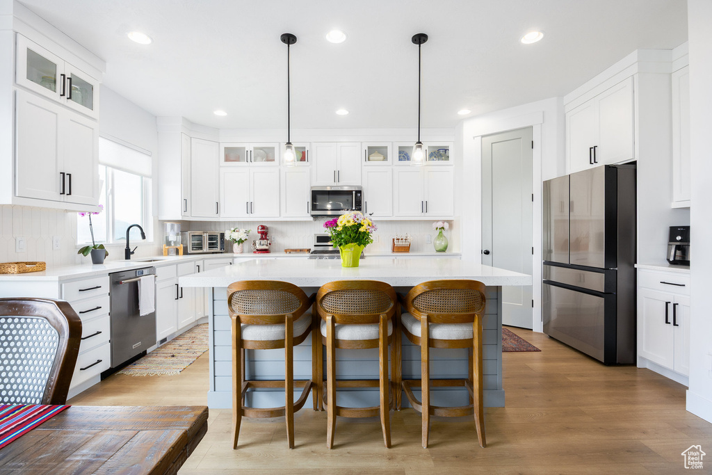 Kitchen featuring appliances with stainless steel finishes, a sink, a center island, tasteful backsplash, and light countertops