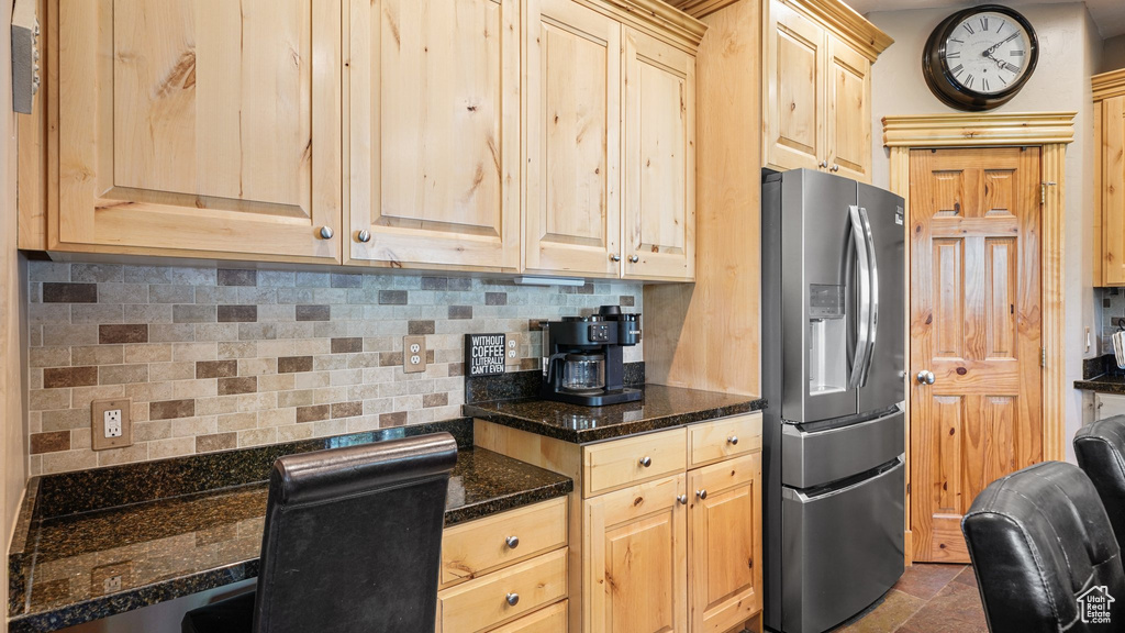 Kitchen featuring stainless steel fridge with ice dispenser, light brown cabinets, backsplash, and dark stone counters
