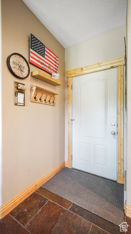 Entryway with stone tile floors, baseboards, and a textured ceiling