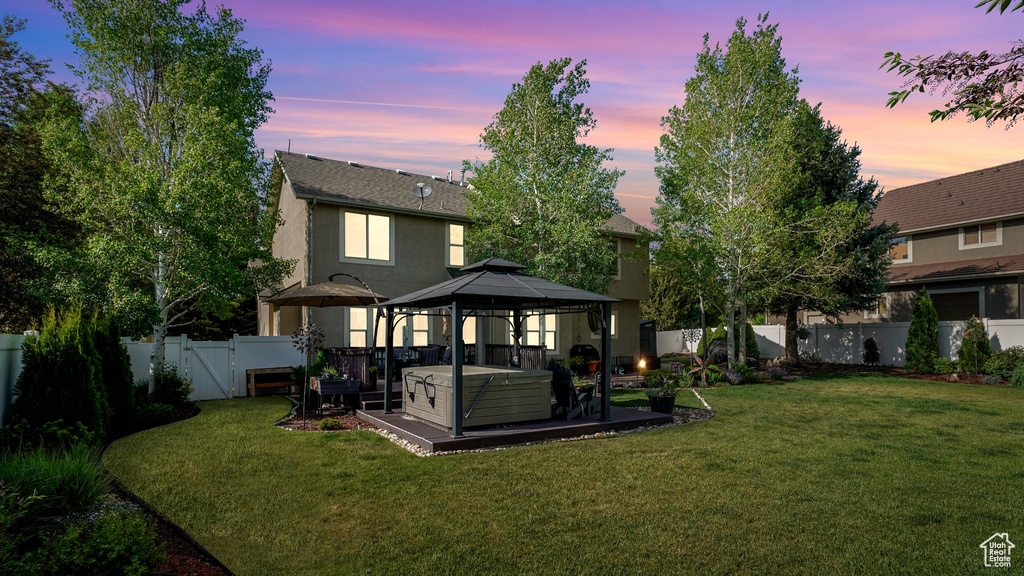 Back of house at dusk featuring a gazebo, a hot tub, and stucco siding