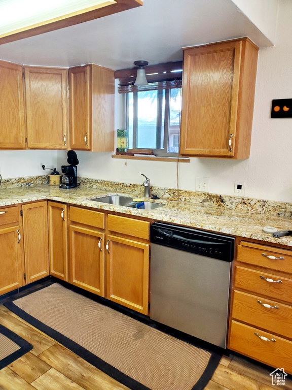 Kitchen featuring dishwasher, a sink, light wood-style floors, and light stone countertops