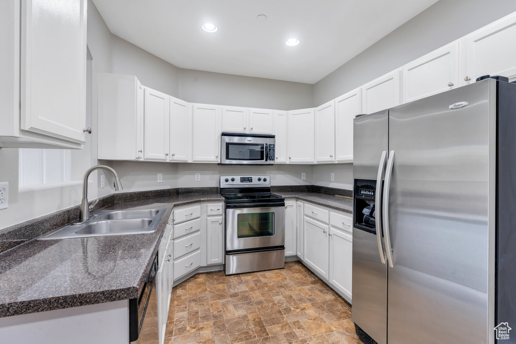 Kitchen featuring stainless steel appliances, a sink, stone finish floors, white cabinets, and recessed lighting
