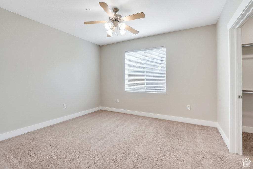 Unfurnished bedroom with a spacious closet, light colored carpet, a closet, baseboards, and ceiling fan