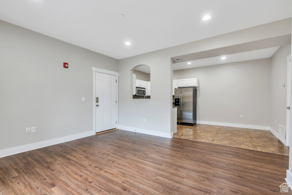 Unfurnished living room with arched walkways, dark wood-style flooring, baseboards, and recessed lighting