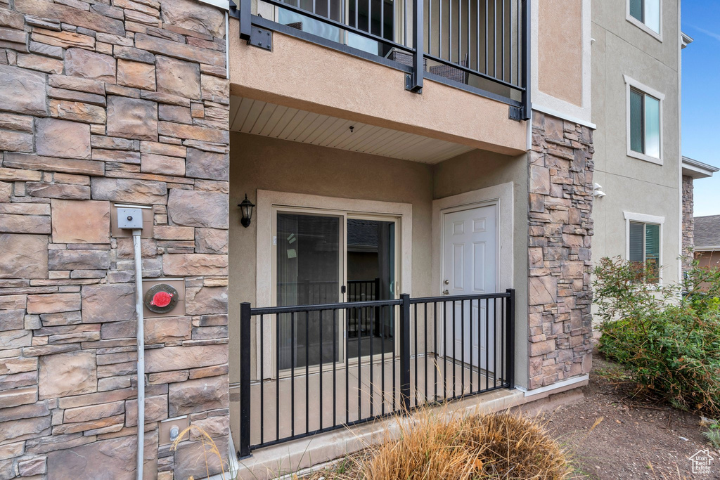 Entrance to property featuring stone siding, stucco siding, and a balcony