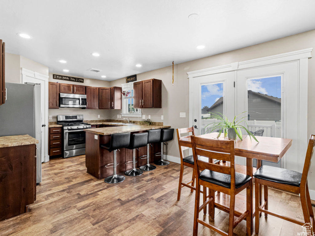 Kitchen with appliances with stainless steel finishes, light wood finished floors, recessed lighting, light countertops, and a breakfast bar