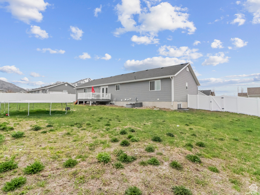 Rear view of house with a gate, a trampoline, a deck, and central AC
