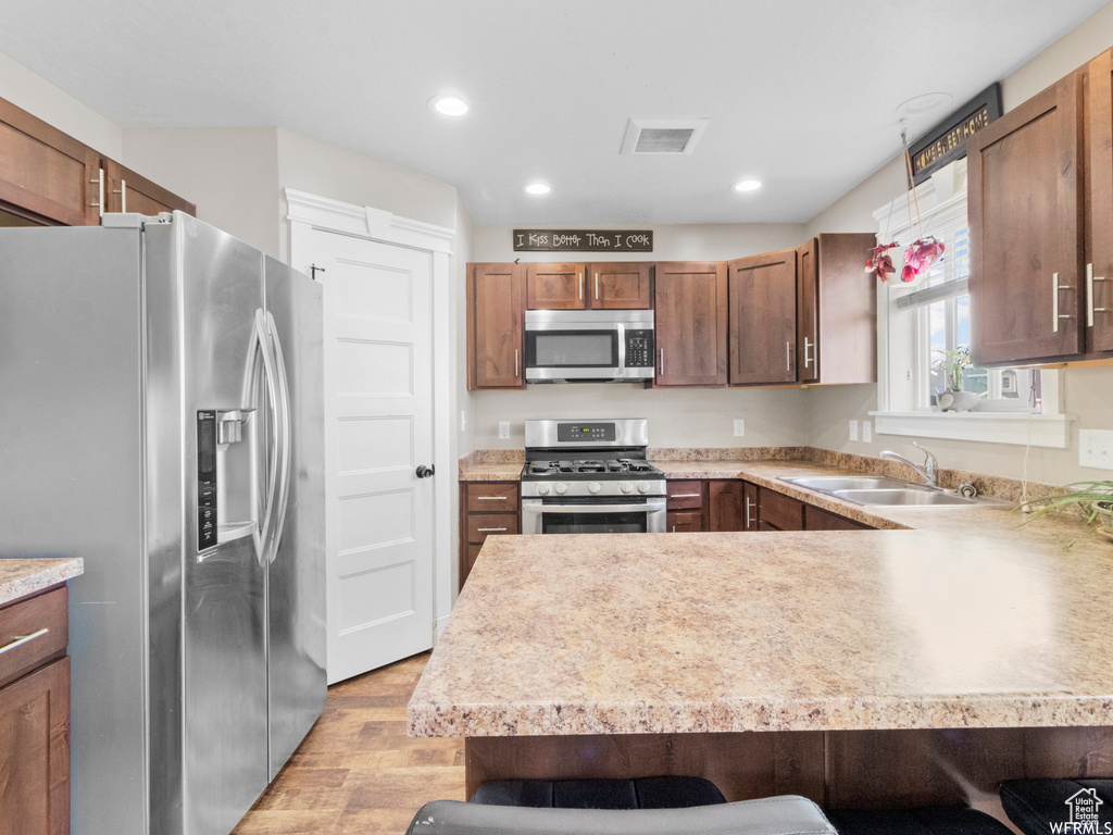 Kitchen with stainless steel appliances, a sink, light wood-type flooring, a kitchen bar, and a peninsula