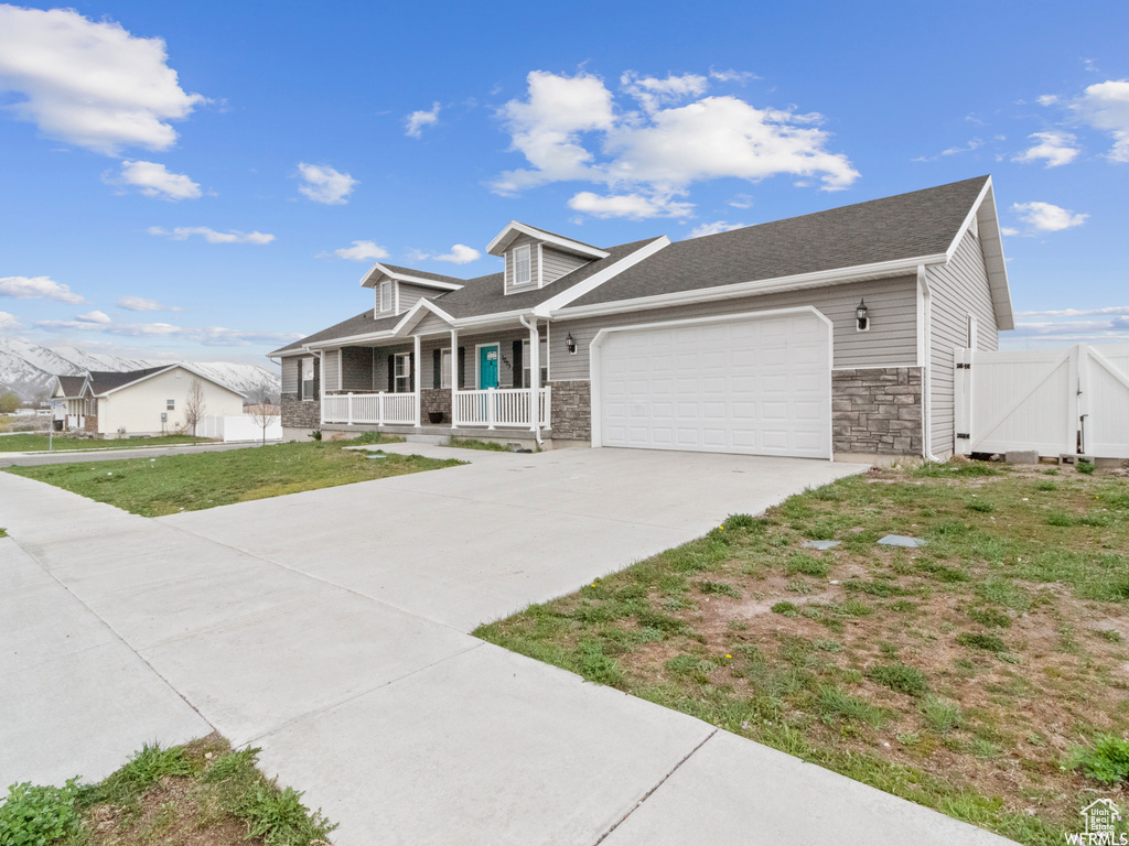 View of front facade featuring a porch, a garage, concrete driveway, and stone siding