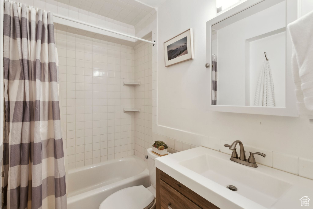 Bathroom with vanity, shower / bathtub combination with curtain, toilet, and tile walls