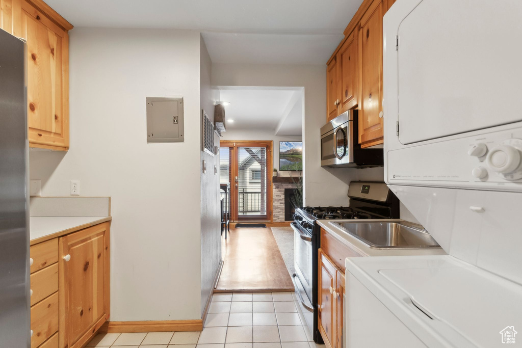 Kitchen with stacked washer / dryer, stainless steel appliances, light countertops, electric panel, and light tile patterned floors