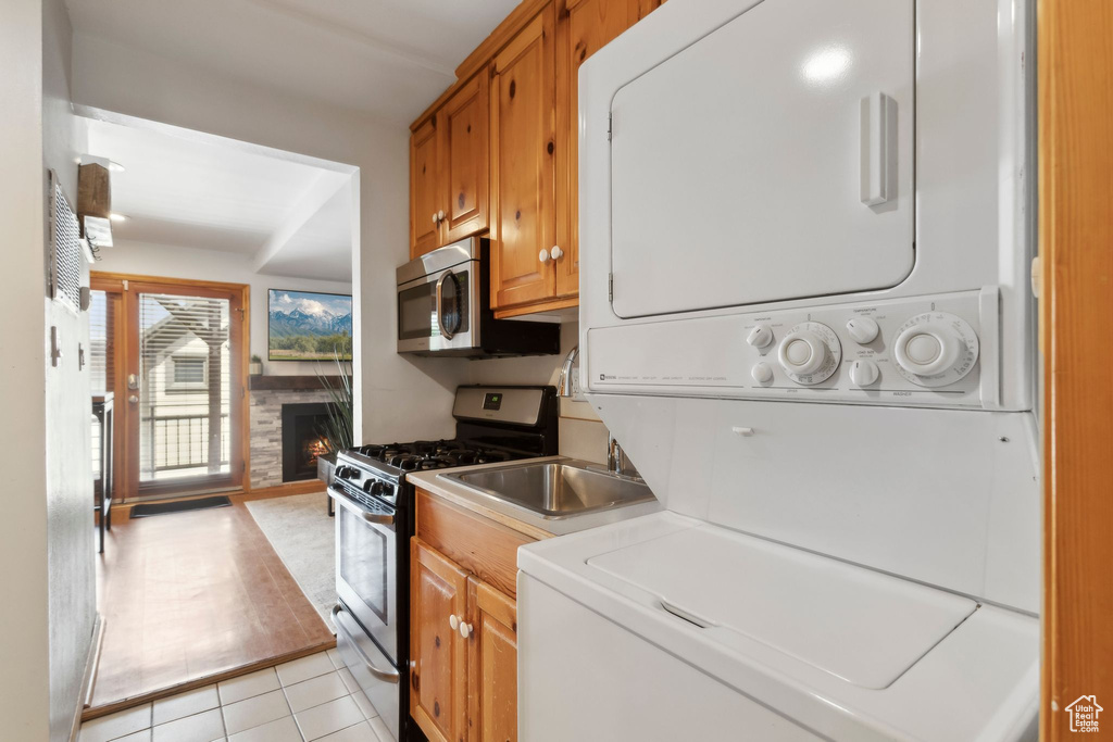 Kitchen with stainless steel appliances, stacked washing machine and dryer, a fireplace, light tile patterned floors, and brown cabinets