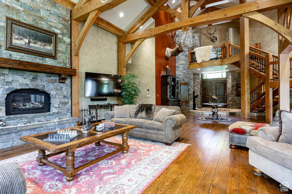 Living room featuring beam ceiling, hardwood / wood-style floors, high vaulted ceiling, a stone fireplace, and stairway