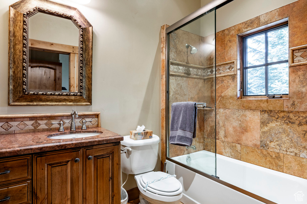 Full bath with toilet, vanity, tasteful backsplash, and shower / bath combination with glass door