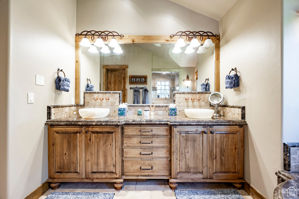 Bathroom with lofted ceiling, decorative backsplash, double vanity, and baseboards