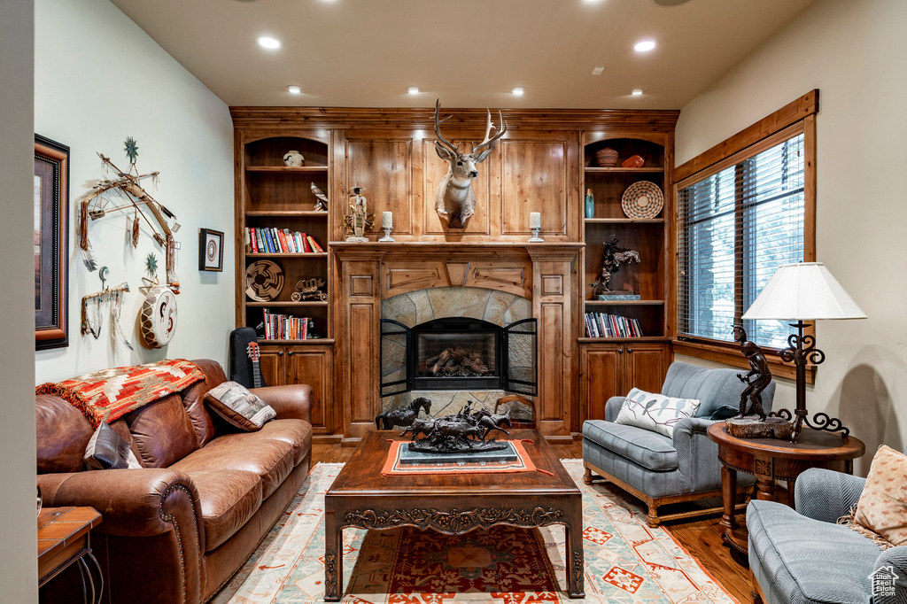 Living area featuring wood finished floors, a stone fireplace, built in shelves, and recessed lighting