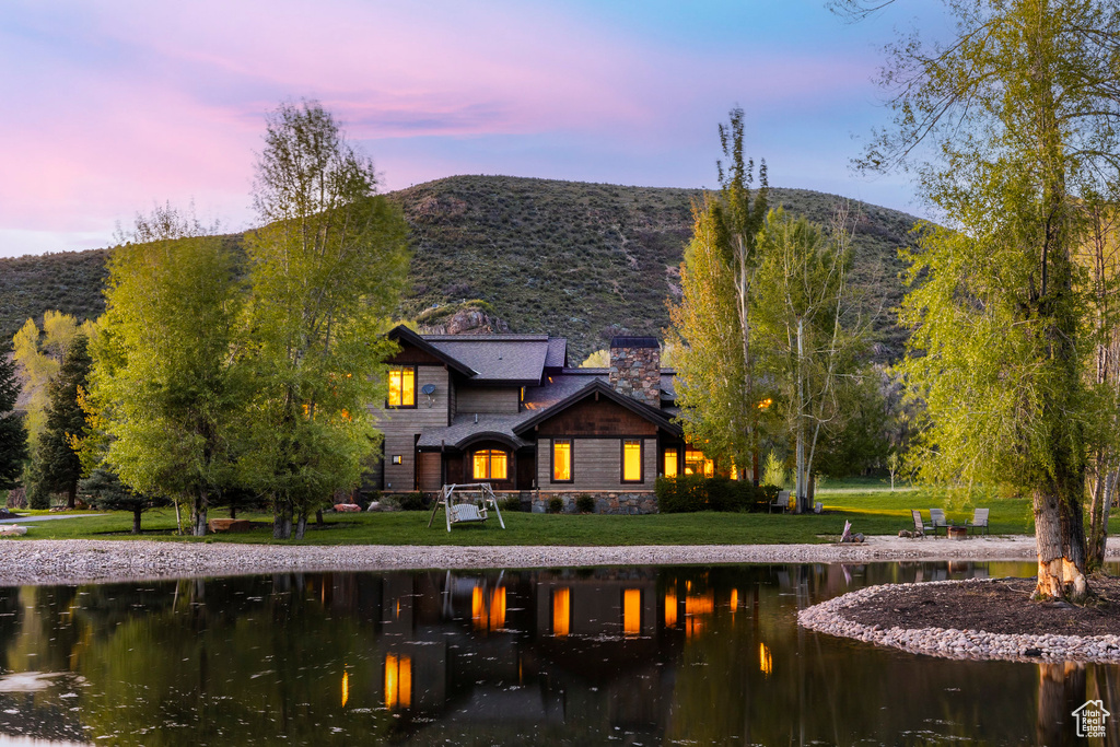 Back of property at dusk featuring a chimney, a lawn, a water and mountain view, and stone siding