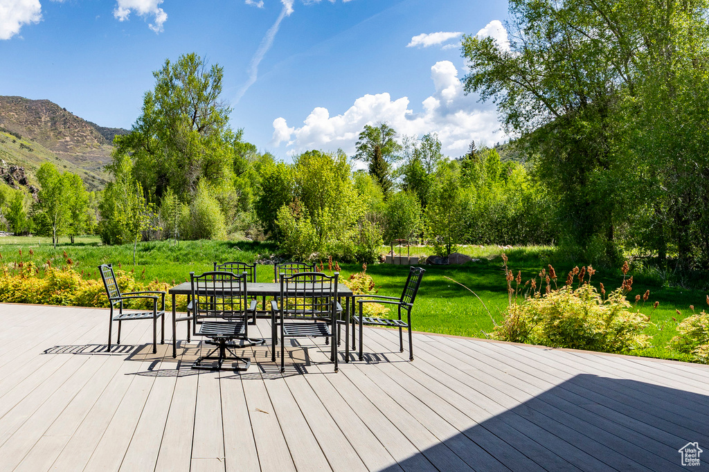 Wooden terrace with outdoor dining area, a lawn, and a mountain view