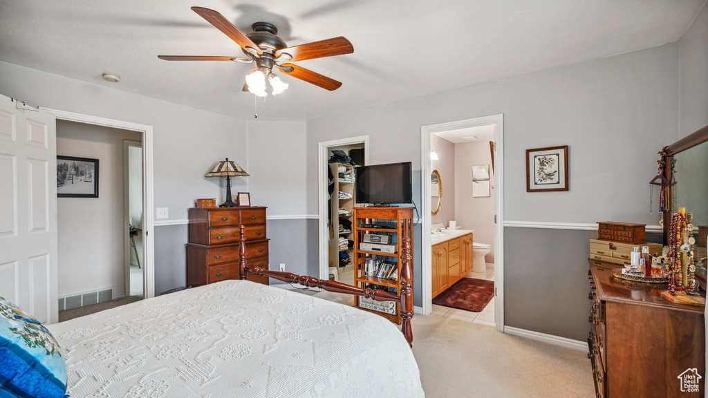 Bedroom with light carpet, a spacious closet, ensuite bath, baseboards, and a ceiling fan