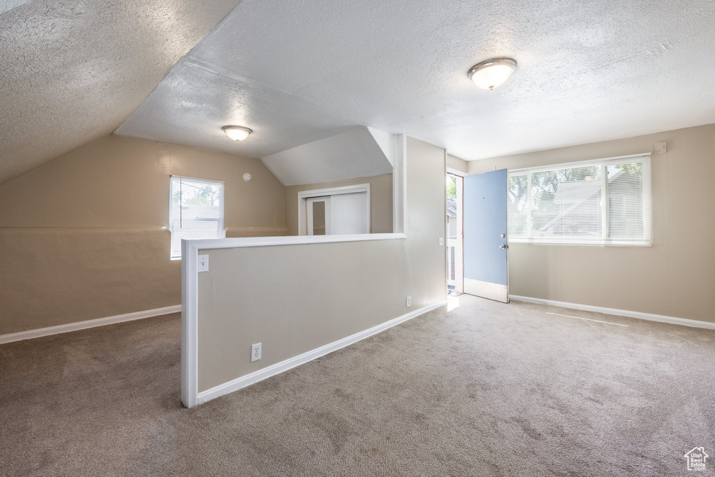 Bonus room featuring a textured ceiling, carpet, baseboards, and vaulted ceiling