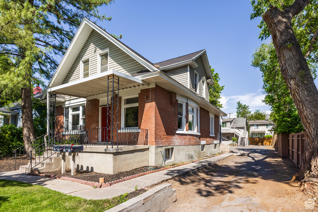 View of front of home featuring covered porch, brick siding, and stairs