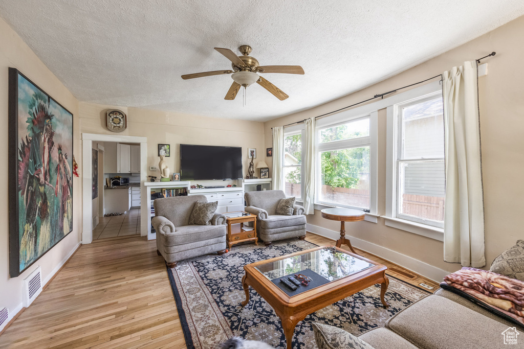 Living area featuring light wood-style flooring, a textured ceiling, ceiling fan, and baseboards