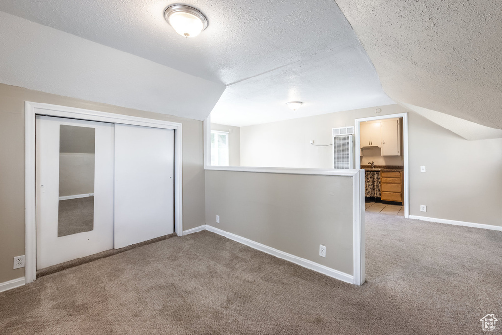Unfurnished bedroom with carpet floors, lofted ceiling, a textured ceiling, a closet, and baseboards