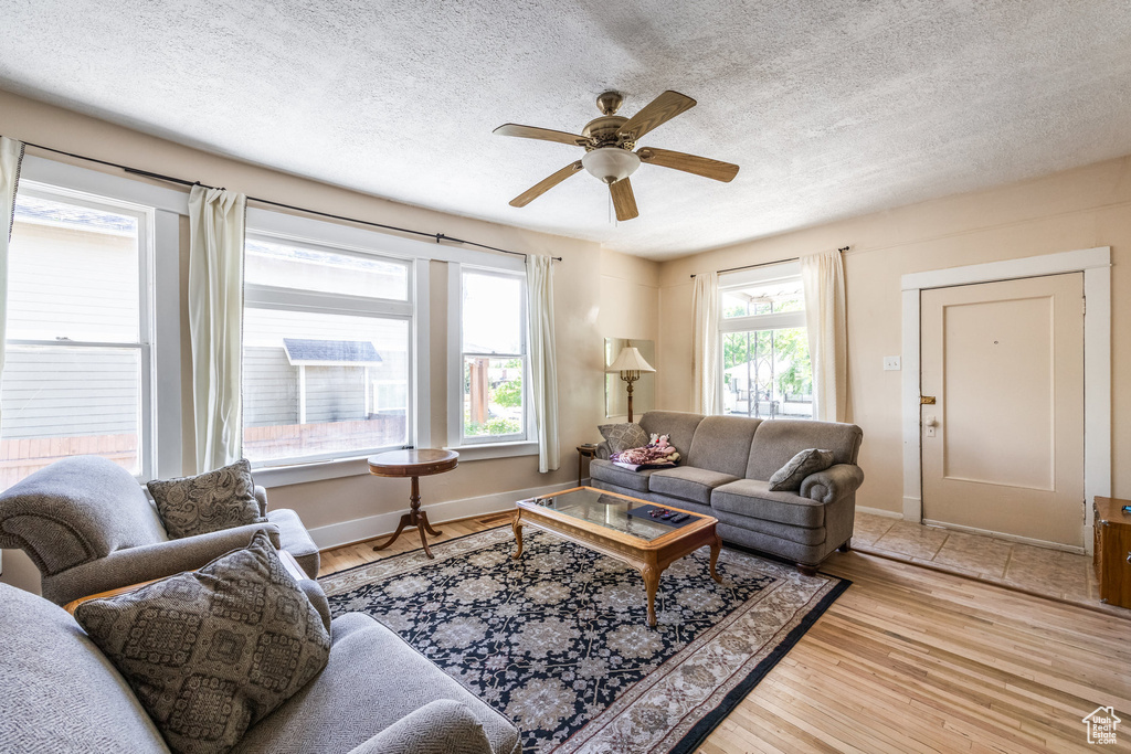 Living area featuring a ceiling fan, a textured ceiling, light wood finished floors, and baseboards