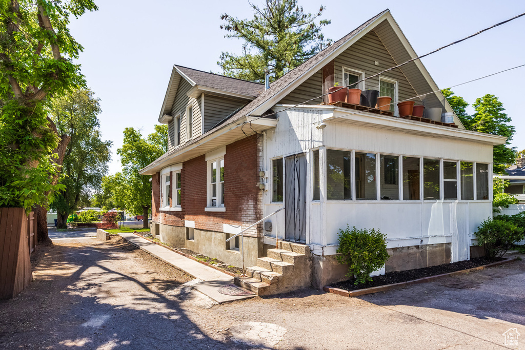 View of front of property featuring a balcony, brick siding, entry steps, and a sunroom