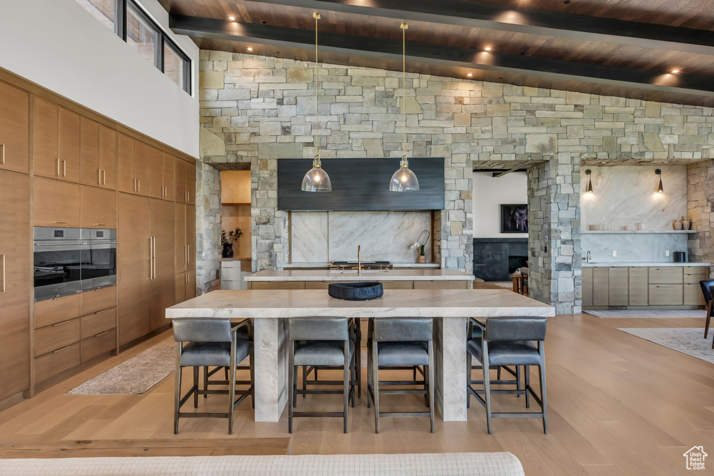 Kitchen with a large island, stainless steel oven, a kitchen breakfast bar, light countertops, and wood ceiling with exposed beams