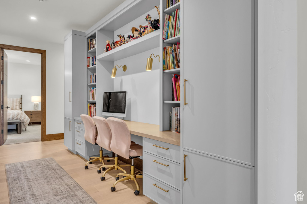 Office area with built in study area, light wood finished floors, recessed lighting, built in shelves, and baseboards