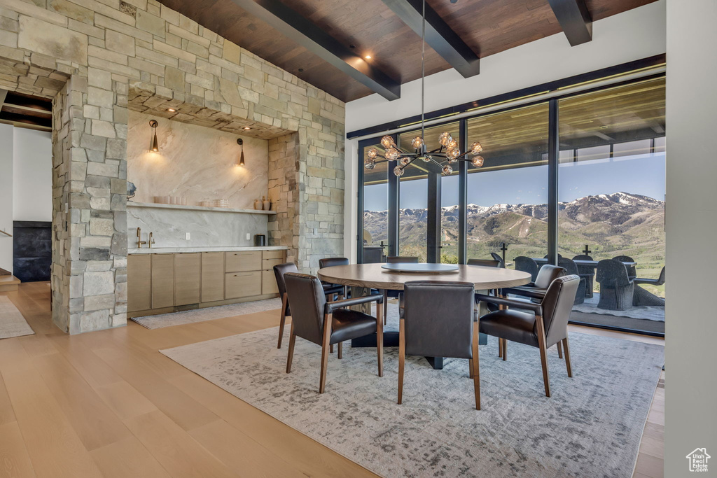 Dining space featuring wooden ceiling with exposed beams, bar with sink, light wood-style floors, a chandelier, and a mountain view