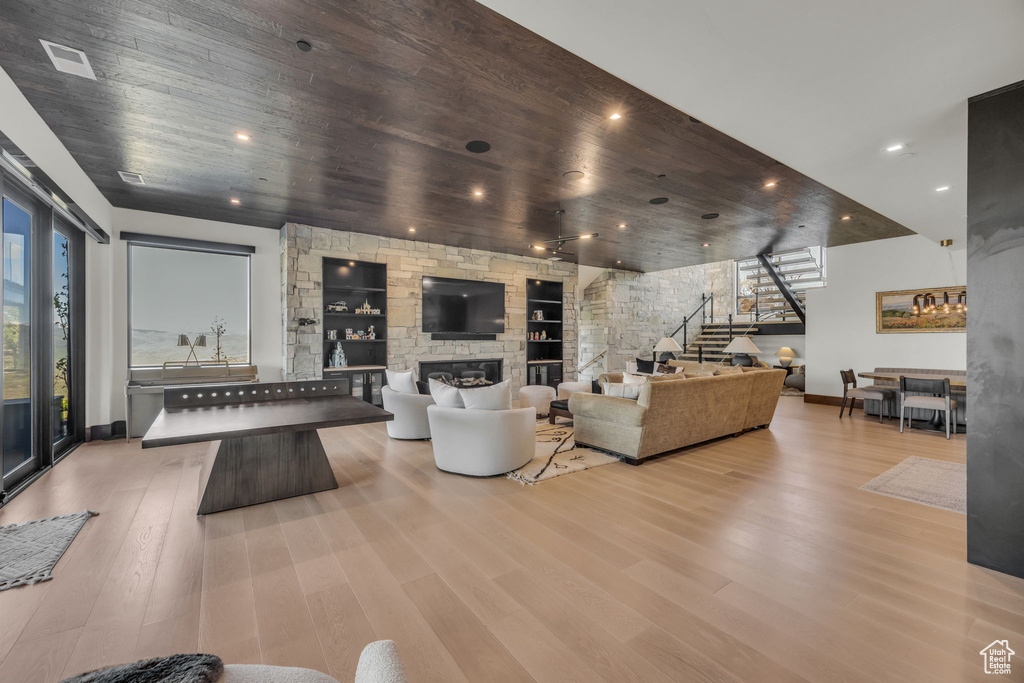 Living room featuring stairway, baseboards, a stone fireplace, wood finished floors, and wooden ceiling