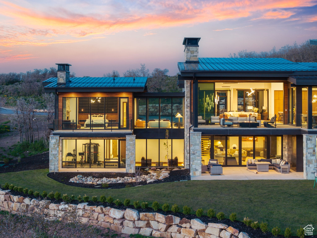 Back of house at dusk featuring an outdoor living space, a standing seam roof, a chimney, a patio area, and metal roof