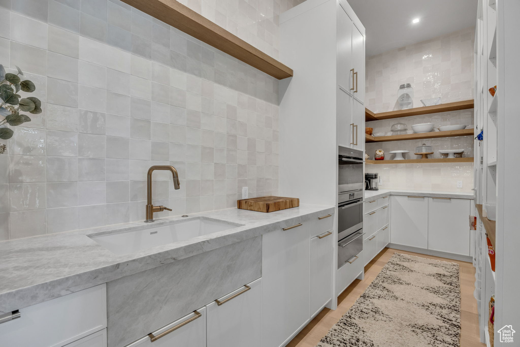 Kitchen with open shelves, a sink, a warming drawer, backsplash, and white cabinets