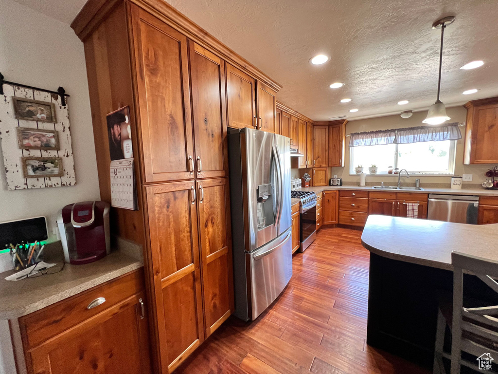 Kitchen featuring appliances with stainless steel finishes, a sink, recessed lighting, brown cabinetry, and wood finished floors