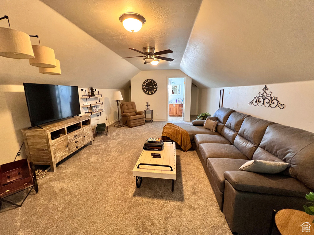 Carpeted living area featuring ceiling fan, vaulted ceiling, and a textured ceiling